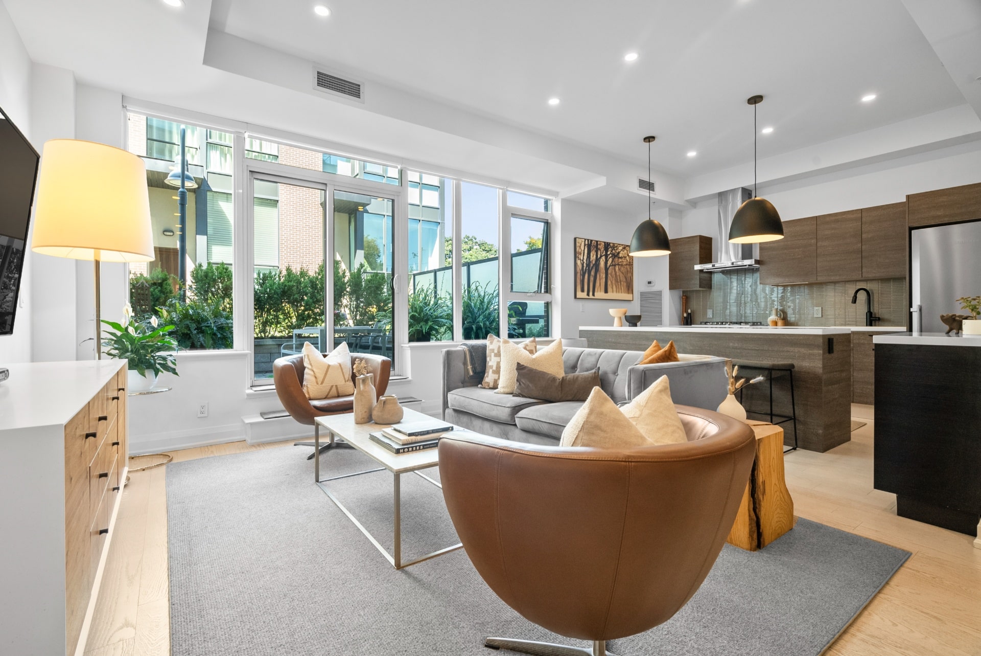 Staged modern living room with grey sofa, leather chairs, and open kitchen. Home staging for real estate sales.