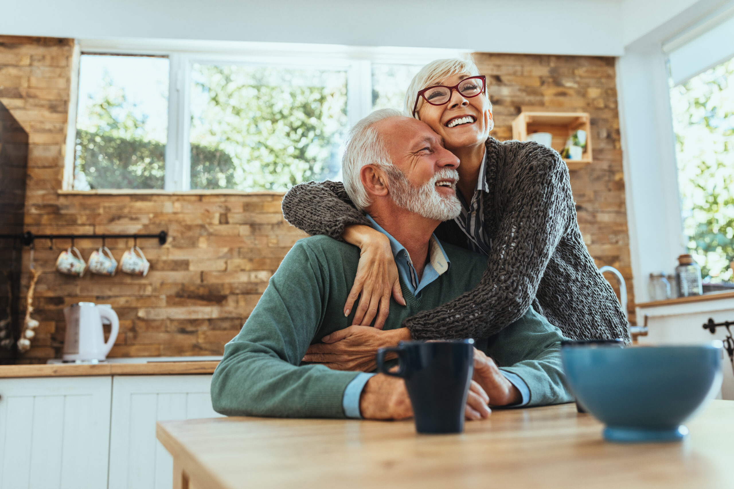 Happy senior couple embracing in kitchen. Design consultation for home buying approach, creating joyful retirement living spaces.