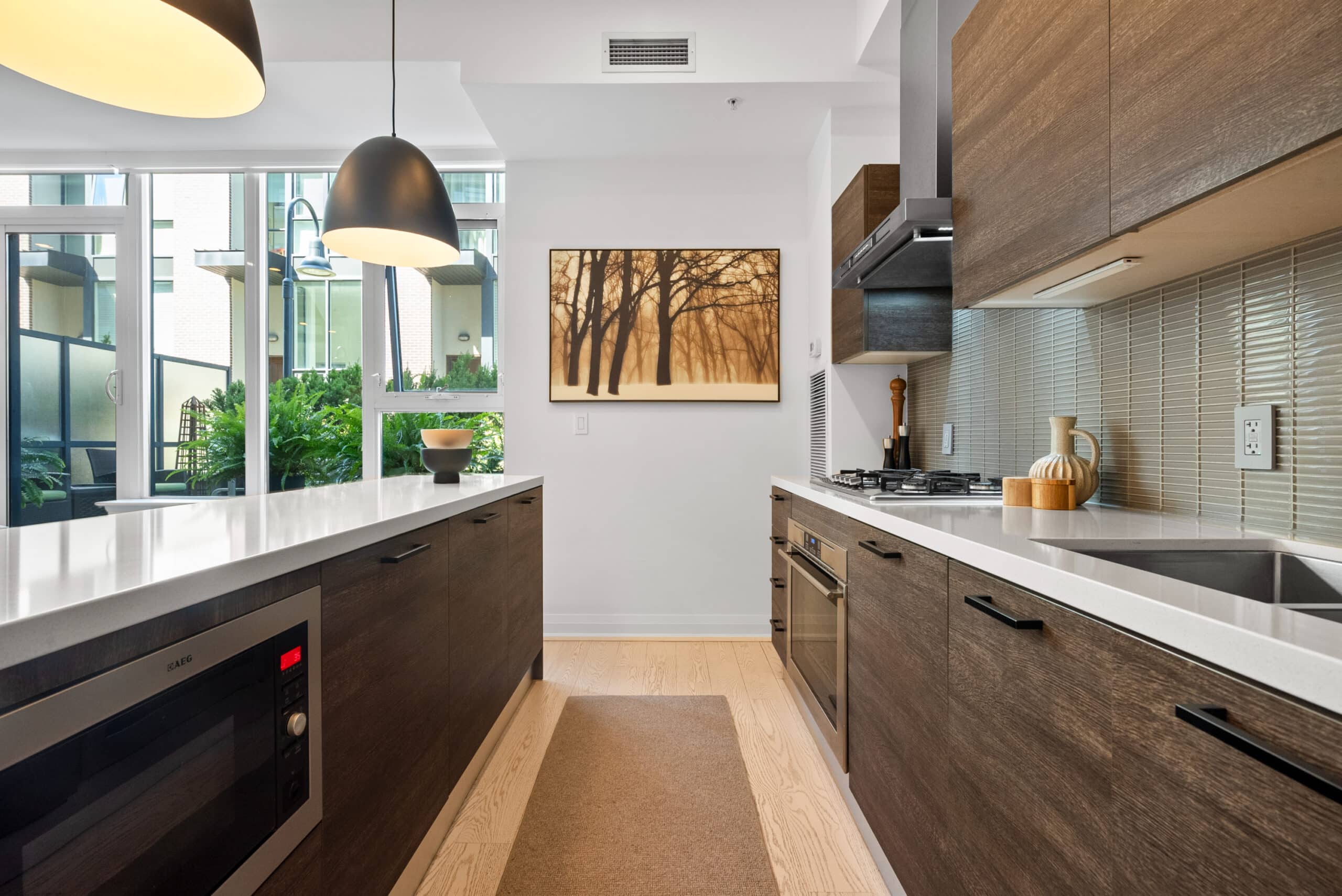 Staged kitchen with wood cabinets, white countertops, modern appliances, and a view to a green courtyard. Kitchen staging.